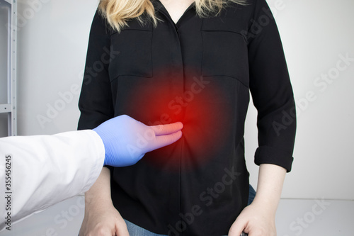 A woman holds on to his stomach. Pain in the abdominal cavity. The concept of diseases of the stomach and digestive system. A gastroenterologist examines the patient. photo