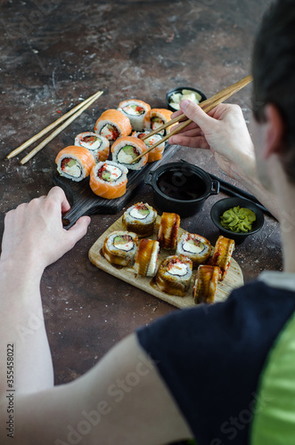 Different Sushi rolls with red fish and eel, wasabi and ginger on a plate on wooden background.