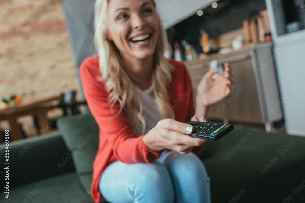 selective focus of cheerful woman laughing while watching tv at home
