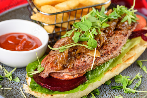 A serving of Steak Sandwich with Beetroot, Lettuce and a side of French Fries and Tomato Sauce