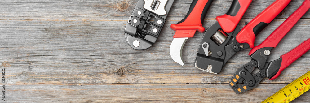 Tools of an electrician-fitter or Builder on a gray wooden table. Construction tools: crimps, knife, gloves and construction tape measure on the table. Top view with space for text. Banner Tools of an electrician-fitter or Builder on a gray wooden table. Construction tools: crimps, knife, gloves and construction tape measure on the table. Top view with space for text. Banner