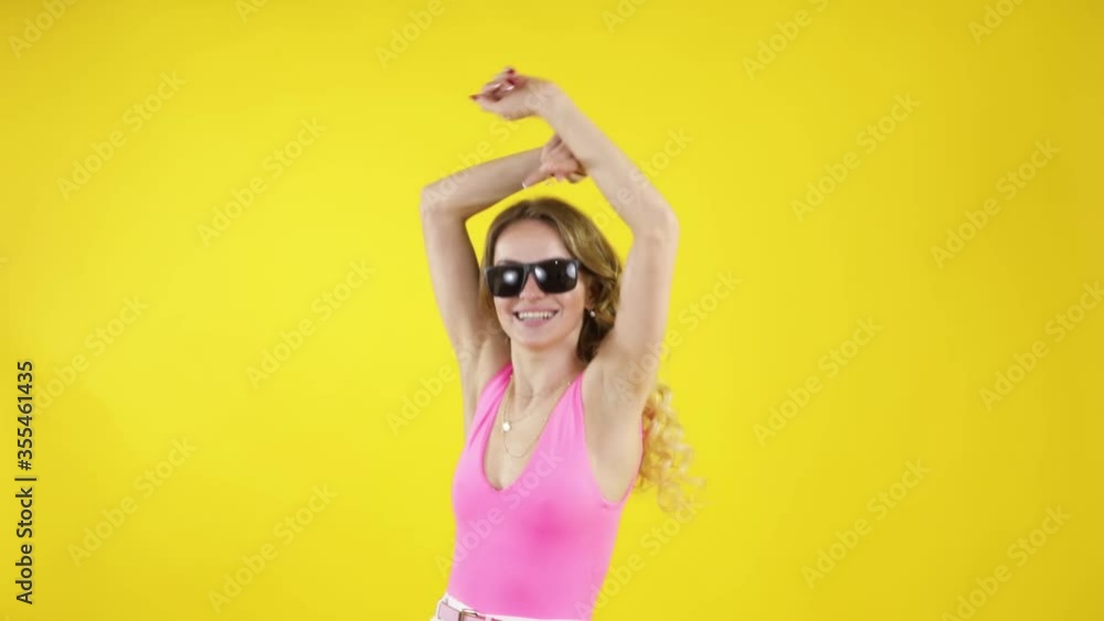 Blond slim model in pink shirt dancing and having fun in fashionable sunglasses on yellow background. Blond slim model in pink shirt dancing and having fun in fashionable sunglasses on yellow background.
