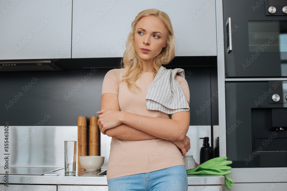 upset housewife with towel on shoulder standing in kitchen and looking away upset housewife with towel on shoulder standing in kitchen and looking away