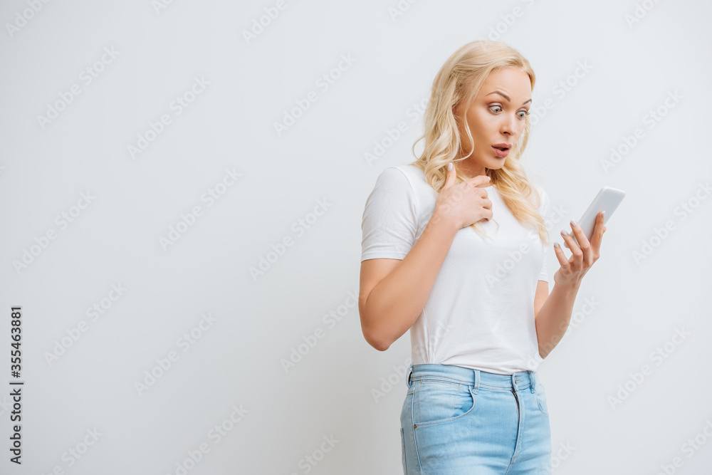 shocked girl holding hand on chest during video chat on smartphone isolated on white shocked girl holding hand on chest during video chat on smartphone isolated on white