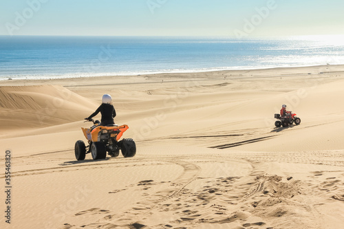 Quad driving people - two happy bikers in sand desert dunes at ocean coast beach, Africa, Namibia, Namib, Walvis Bay, Swakopmund.