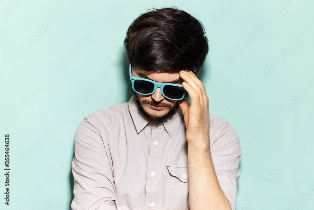 Portrait of young sad guy wearing shades on background of aqua menthe color. Portrait of young sad guy wearing shades on background of aqua menthe color.