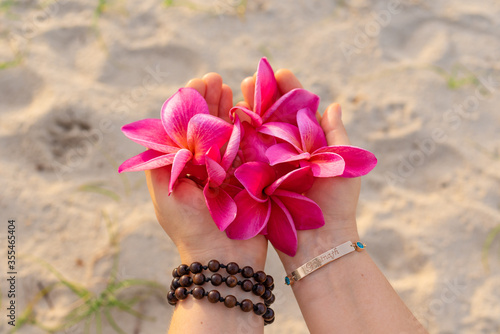 person holds exotic frangipani flowers in his hands, a golden bracelet with topazes, the word "Gopinath"on the bracelet translated from Sanskrit means "Perfect sweetheart", a tropical plumeria flower