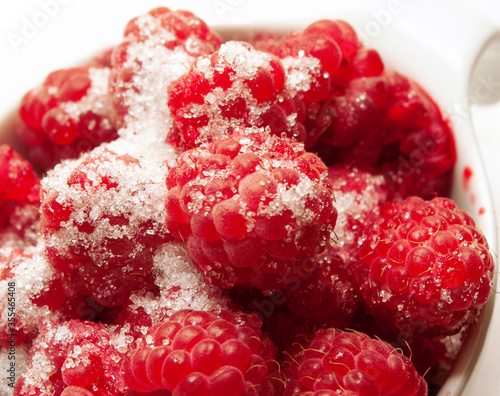 Ripe raspberries with sugar around white background. close up.