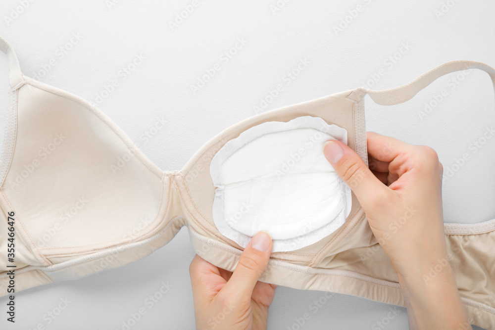 Young mother hand putting white breast pad in bra on light gray table  background. Clothes protection in breastfeeding time. Closeup. Point of  view shot. Top down view. Stock Photo | Adobe Stock