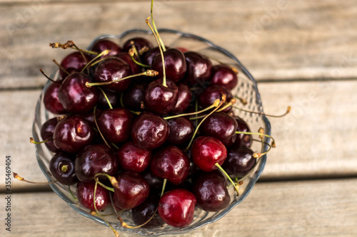 A transparent vase with cherries stands on a wooden bench.