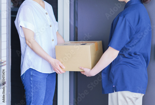 ネット通販の配達小包を届ける配達員とマンションの玄関先で受け取る主婦