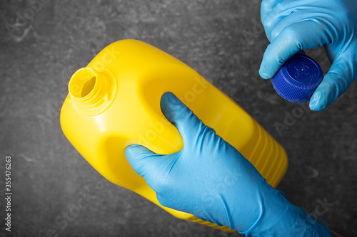 Fototapeta Human hand in protective glove holding a yellow bleach bottle. Disinfection concept