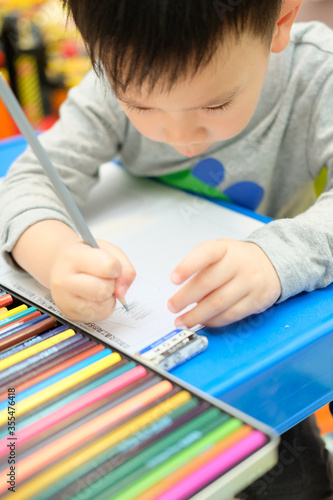 A boy is drawing a picture with color pencil at home.