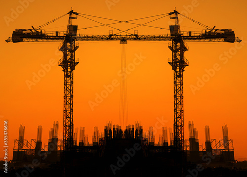 The silhouette of the tower crane to work at a construction site with the background of the sunset sky light gold.