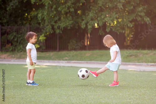 Toddler children  boy and girl  playing soccer together at football field. Little friends kicking ball in summer day standing at stadium in sun light. Friendship and sports for kids concept