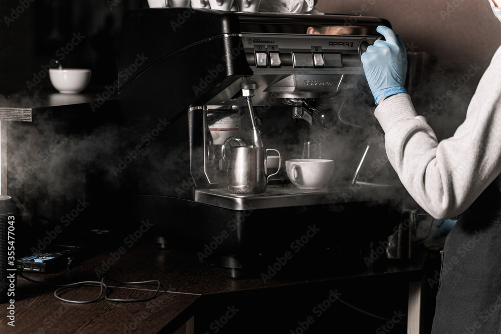 Coffee shop after quarantine. Barista girl in medical gloves releases steam from a coffee machine