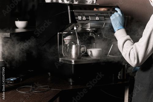 Coffee shop after quarantine. Barista girl in medical gloves releases steam from a coffee machine
