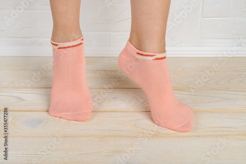 Woman feet in short pink cotton socks standing on toes on a white wood floor. Stand on tiptoe in low rise sports socks close-up.