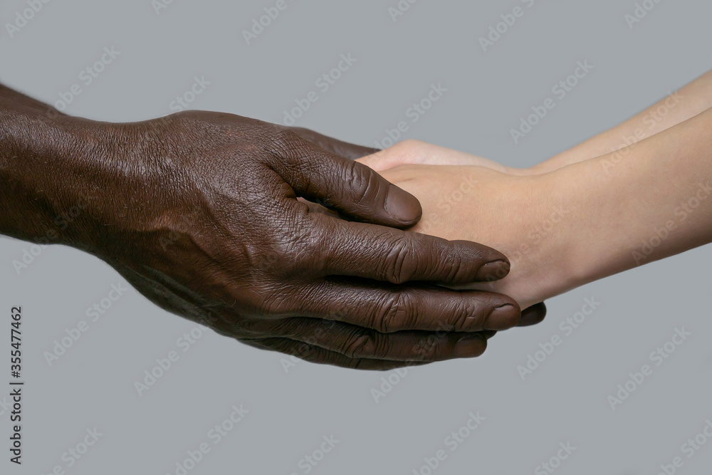 Fototapeta premium Black male hands hold white female human hands in their palms. The concept of inter-racial friendship, love, respect, and the fight against racism. Copy of the space, gray isolated background.
