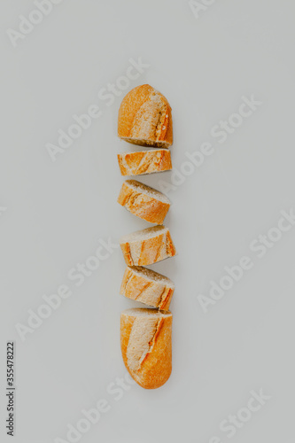 A flat lay of a baguette bread cut up on a light pastel grey background