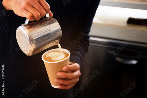 Professional barista pouring steamed milk into coffee paper cup making beautiful coffee. 
