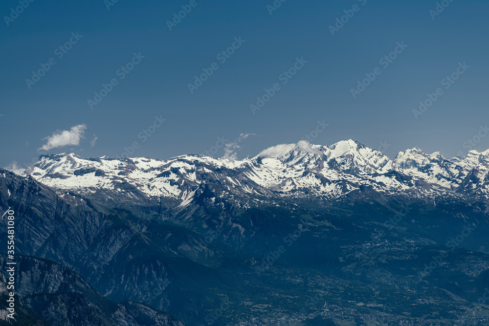 Alpine mountains, meadows and forests on a background of blue sky with clouds.