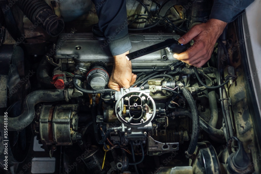 Fototapeta premium A mechanic's hands fix a car engine. Carburetor exposed while being repaired. Service maintenance.