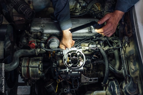 A mechanic's hands fix a car engine. Carburetor exposed while being repaired. Service maintenance.