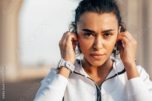 Close up portrait of sweated sportswoman adjusting her earphones during a workout 