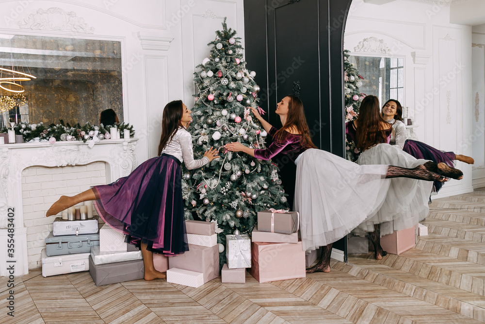two girls in beautiful dresses are dancing near the New Year tree