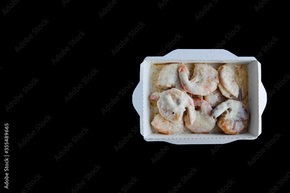food with home delivery, shrimp in cream sauce in a disposable box on a black background