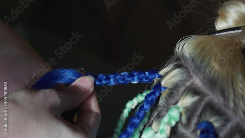 Hands of a young girl braids blue African braids. Head of a woman at the hairdresser closeup. photo