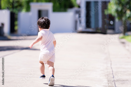 Asian boy wearing bright Romper suit is playing on streets in front of house. Turn back to photographer. Run cheerful and bright. Concept strong child wants to leave the house from a virus outbreak.