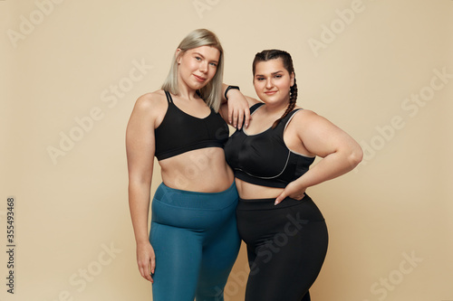 Body Positive. Plus Size Models Portrait. Confident Full-Figured Women In Sport Clothes Against Beige Background. Fitness For Active Lifestyle. photo