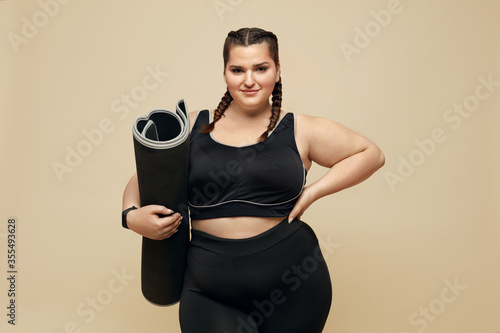 Fitness. Plus Size Model In Black Sportswear Portrait. Full-Figured Woman Holding Pilates Mat. Body Positive And Sport As Lifestyle.