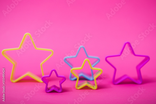 Plastic molds of blue and yellow colors for making cookies in the shape of a star on a pink background. Culinary or party concept. Flat lay with copyspace.