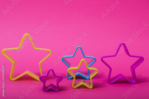 Plastic molds of blue and yellow colors for making cookies in the shape of a star on a pink background. Culinary or party concept. Flat lay with copyspace.
