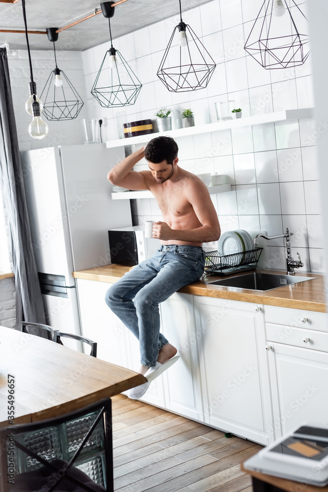 shirtless man holding cup of coffee on kitchen in morning