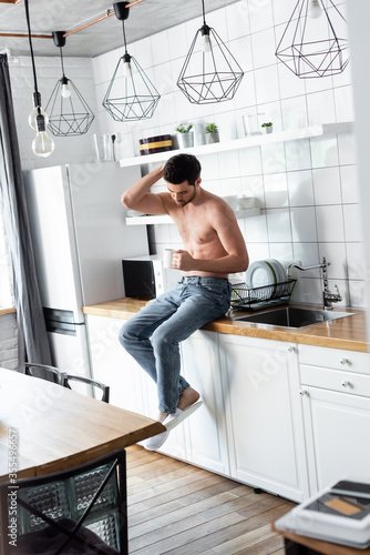 shirtless man holding cup of coffee on kitchen in morning © LIGHTFIELD STUDIOS