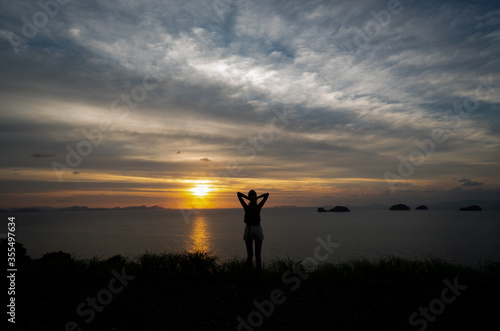 Silhouette of a woman watches sunset over a sea or ocean on a tropical island. © Volodymyr