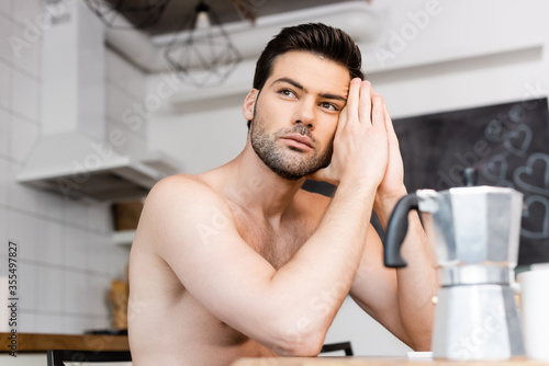 thoughtful shirtless sad man sitting on kitchen with coffee pot