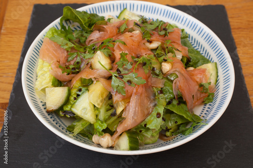 A salad with smoked salmon and mixed greens with a salad dressing and mixed herbs