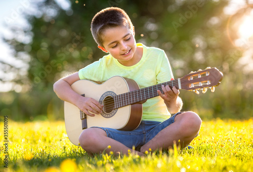 Boy playing acoustic guitar in a field at sunset