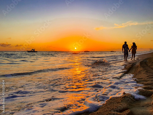 Couple's silhouette on the beach at sunset with boat in the background. Grand Bahia Principe beach in Punta Cana, Dominican Republic.