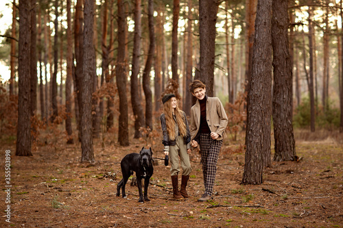 Girl and boy walk with a dog Cane corso in the forest and have a fun. Children stand near a tree and hold a dog on a leash.