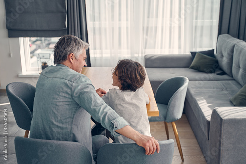 Grey haired man and little child sitting in living room
