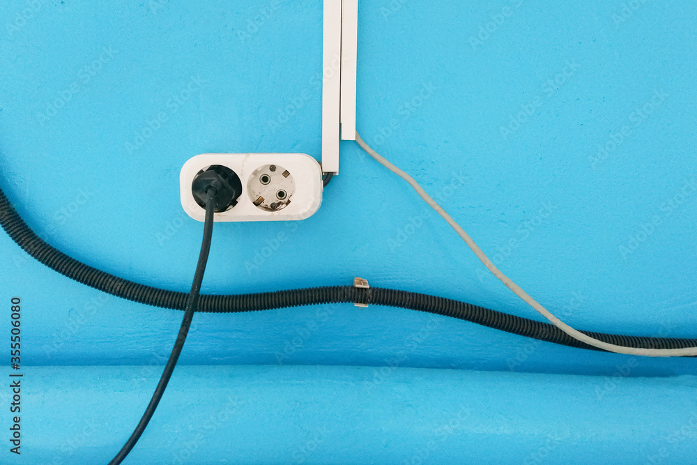 electric plug socket with wires sticking out on a blue background. Violation of electrical safety in the building. Overload-Active power consumption. tangled wires risk of short circuit and fire