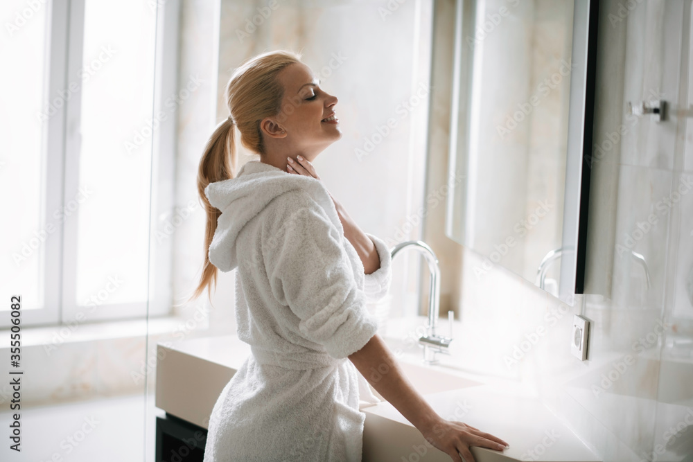 Beautiful woman in bathrobe use the cream for the body. Young woman enjoying in hotel. Beautiful woman in bathrobe use the cream for the body. Young woman enjoying in hotel.