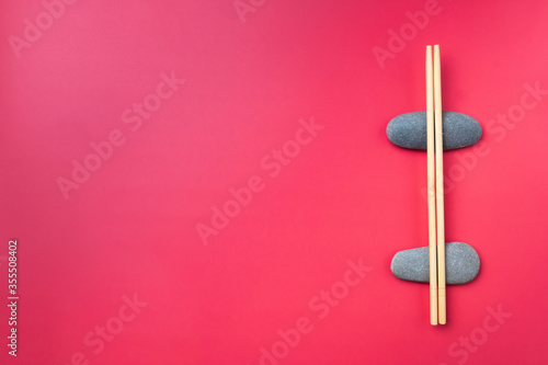 Flat lay. Light wooden chopsticks lie on oval stones on a pink background. Traditional Asian cutlery. Copy space