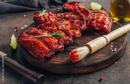 Mexican barbecued ribs seasoned with a spicy tomato sauce served on a wooden chopping board on a dark background.